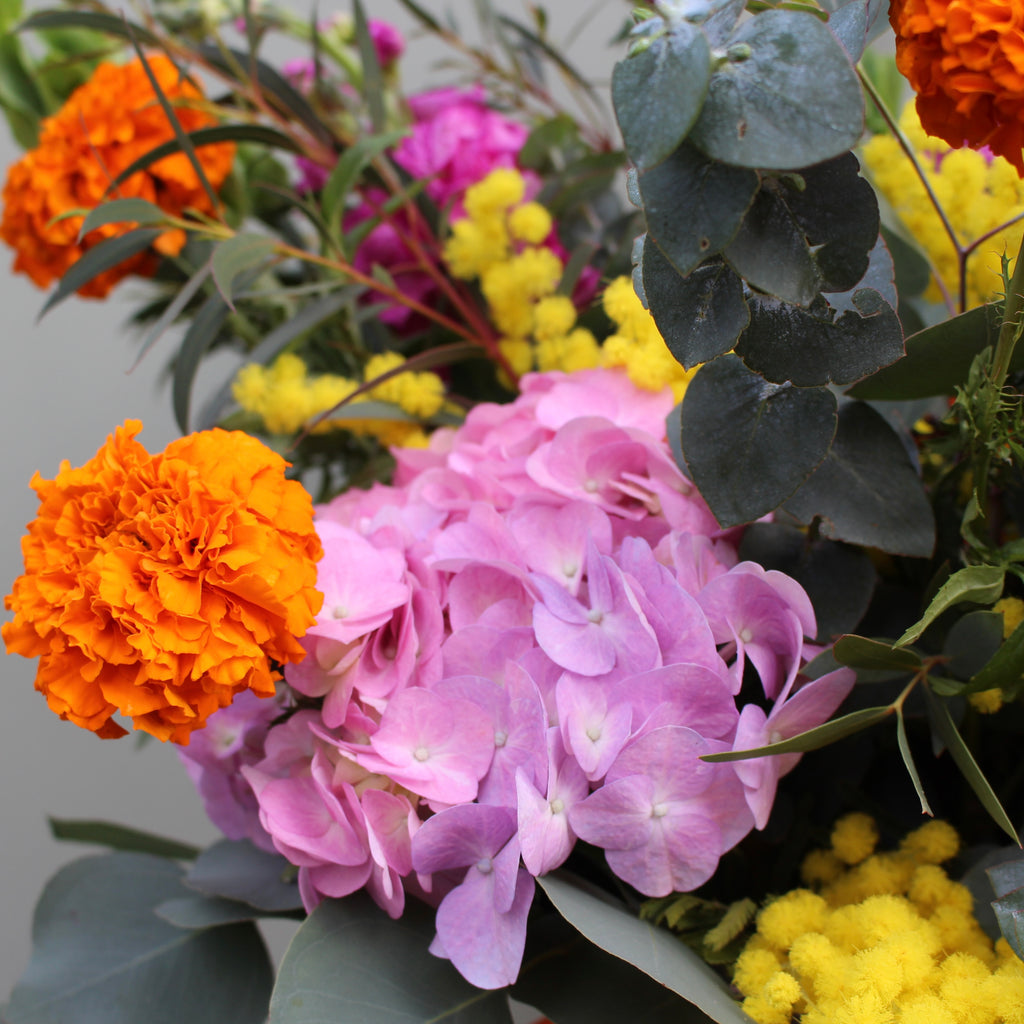 Lorelai (A juicy, bright creation containing marigolds, mimosa, hydrangea, stocks and mollucella in cerise pink, yellow and orange.)