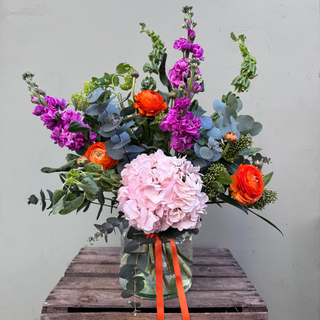 Lorelai (A juicy, bright creation containing ranunculus, skimmia, viburnum, hydrangea, stocks and mollucella in cerise pink, lime green and orange.)
