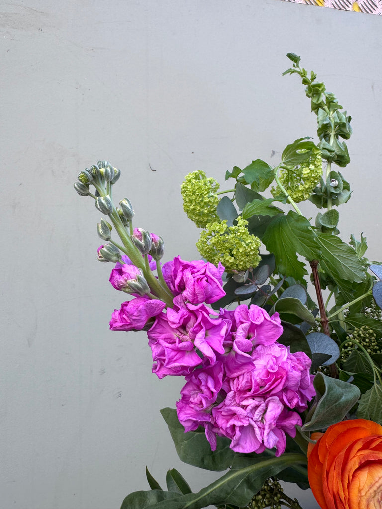 Lorelai (A juicy, bright creation containing ranunculus, skimmia, viburnum, hydrangea, stocks and mollucella in cerise pink, lime green and orange.)